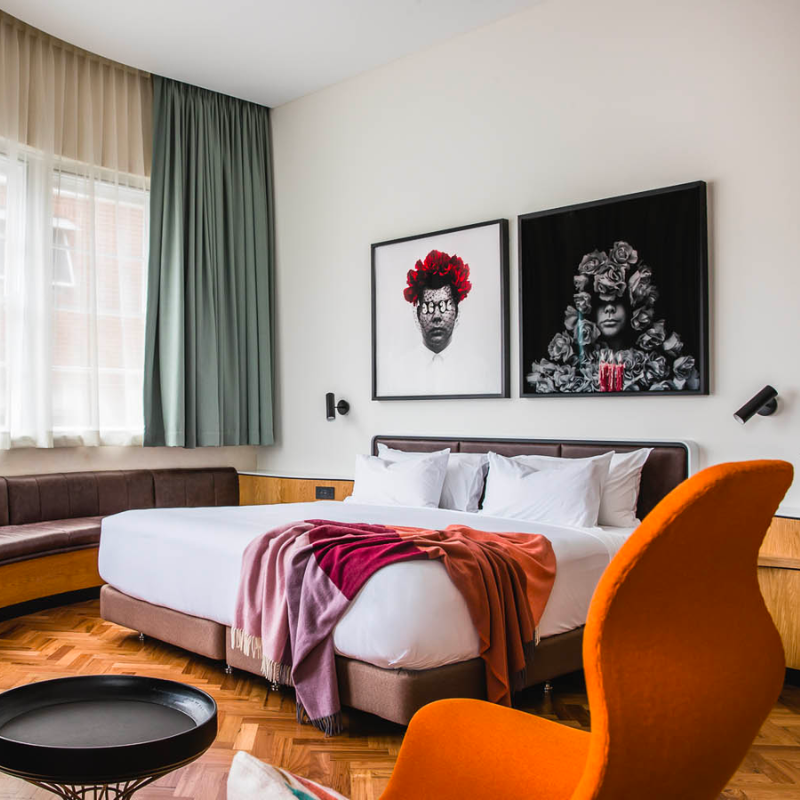 A luxurious hotel room with king bed, orange armchair and sofa